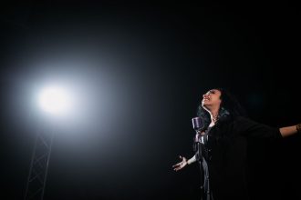 Cantora country se apresenta ao vivo sob um holofote em um palco escuro.